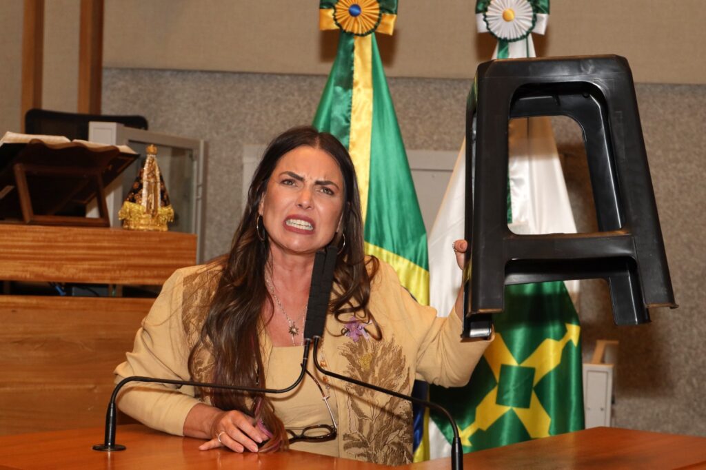 Foto mostra a deputada Paula Belmonte segurando um banco de plástico com expressão de cobrança. Ela está no Plenário da CLDF